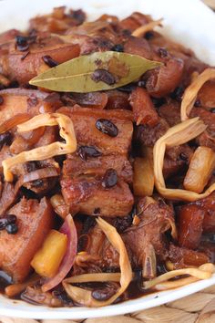 a white bowl filled with meat and onions on top of a wooden table next to a green leaf