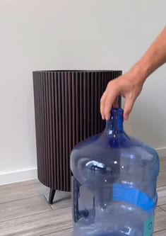 a person is holding a large blue water bottle on the floor next to a heater