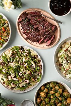 a table topped with plates filled with different types of food next to bowls of salad