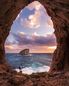 a person standing in the middle of a cave looking out at the ocean and an island