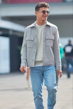 a man walking down the street with his foot in the air while wearing sunglasses and a gray jacket