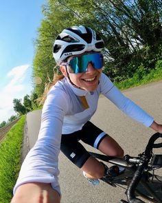 a woman is riding her bike down the road wearing goggles and smiling at the camera