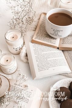 an open book and cup of coffee sit on a table next to some cookies, candles and flowers