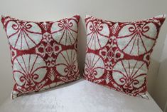 two red and white pillows sitting on top of a bed next to each other in front of a wall