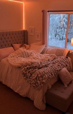 a bed with a blanket and pillows on it in front of a window that has snow outside