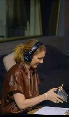 a woman sitting at a desk wearing headphones and writing on a piece of paper