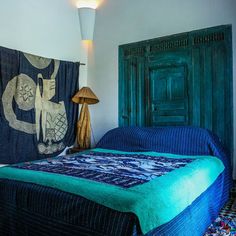 a bed with a blue blanket on top of it next to a lamp and wooden door