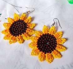 two yellow and black beaded sunflowers are hanging from earrings on a table