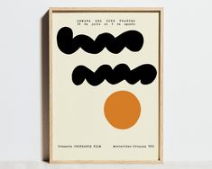 an orange and black poster hanging on a wall next to a white wall with a wooden frame