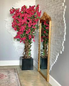 two vases with pink flowers are next to a mirror on the floor in front of a brick wall