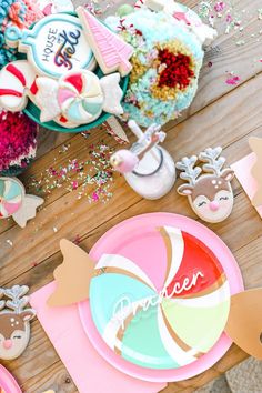 a wooden table topped with lots of colorful plates and desserts covered in frosting