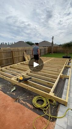 a man standing on top of a wooden deck in the middle of a yard next to a fence