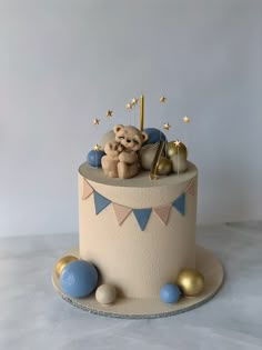 a birthday cake with a teddy bear on top and decorations around the base, including stars