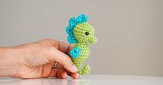 a hand holding a tiny crocheted green and blue seahorse