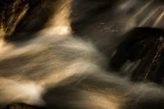 the water is rushing over the rocks in the river at night, with light coming from behind it