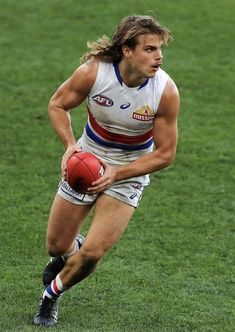 a male afl player is running with the ball in his hand and holding it out