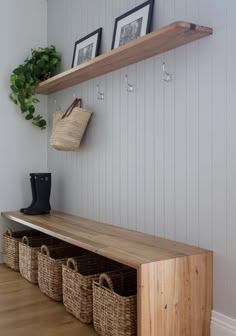 a wooden bench with baskets on it next to a wall mounted coat rack and two framed pictures