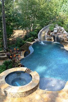 an outdoor swimming pool surrounded by trees and water features a slide that leads to a waterfall