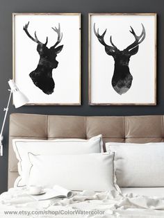 two framed deer head prints on the wall above a bed with white linens and pillows