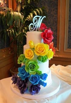 a multi - tiered cake decorated with flowers and the letter m on top is sitting on a table