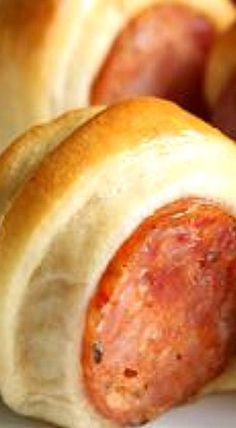 two sausages wrapped in bread on a plate with other food items behind them,