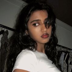 a woman with long black hair wearing a white t - shirt and looking at the camera