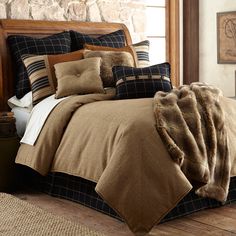 a bed covered in brown and black comforter next to a stone wall with windows