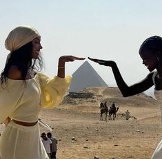 two women in white dresses pointing at each other with pyramids in the back ground