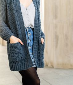 a woman standing on the sidewalk wearing a blue cardigan sweater and black tights