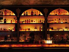 a dimly lit bar with lots of bottles on the shelves and lights above it at night