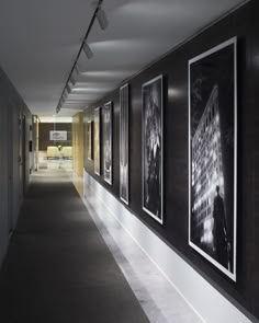 a long hallway with black and white pictures on the wall, along with dark carpeting