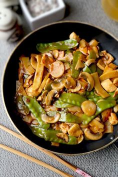 stir fry with mushrooms and green beans in a black bowl next to chopsticks