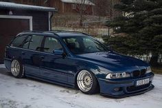 a blue car parked in the snow next to a garage with trees and buildings behind it