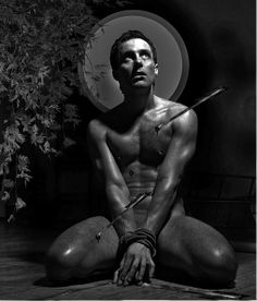 a shirtless man sitting on the floor with two swords in his hands