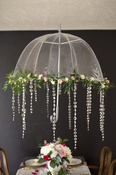 an umbrella is hanging over a table with flowers and greenery on the tablecloth