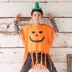 a young boy dressed up as a pumpkin wearing a green hat and holding his hands behind his head