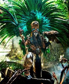 a man dressed as a jaguar with feathers on his head standing in front of trees