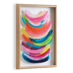 an abstract painting with multicolored feathers in a wooden frame on a white wall