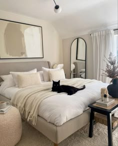 a black cat laying on top of a white bed in a bedroom next to a window