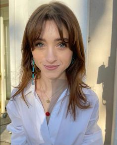 a woman with brown hair and blue earrings is posing for a photo in front of a building