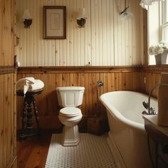 a white toilet sitting next to a bath tub in a bathroom on top of a hard wood floor