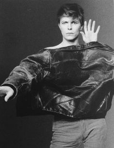 a black and white photo of a man in a leather jacket holding his hands up