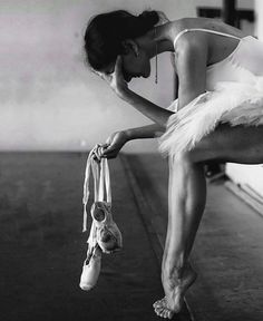 a black and white photo of a ballerina tying her ballet shoes with one hand