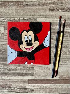 a mickey mouse painting next to a pencil on a wooden surface with a red background