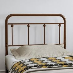 a bed with a white and yellow blanket on it's headboard next to a wall