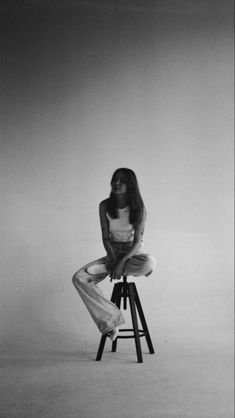 a black and white photo of a woman sitting on a stool