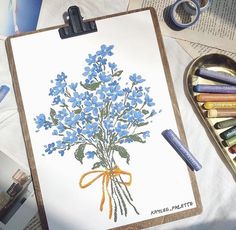 a drawing with blue flowers on it next to crayons and colored pencils