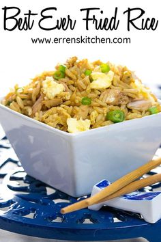 a white bowl filled with rice and vegetables next to chopsticks on a blue plate