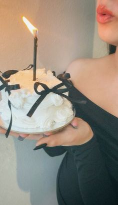 a woman holding a cake with a lit candle on it and tied to the side