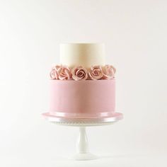 a three tiered cake with white and pink frosting roses on top, sitting on a pedestal